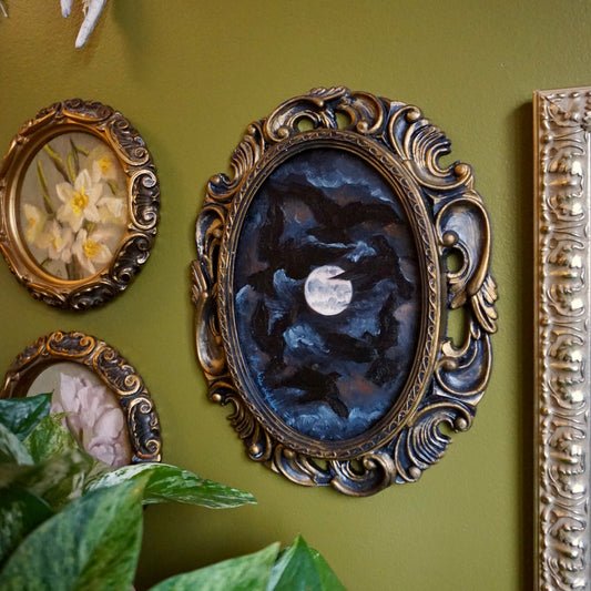 Decorative wall with ornate gold frames containing artwork on a green wall.